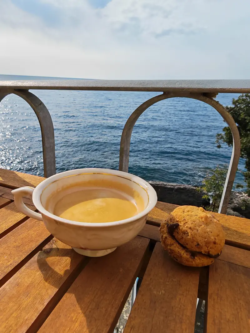 A cup of coffee in the spring sun, on a table by the railing above the sea