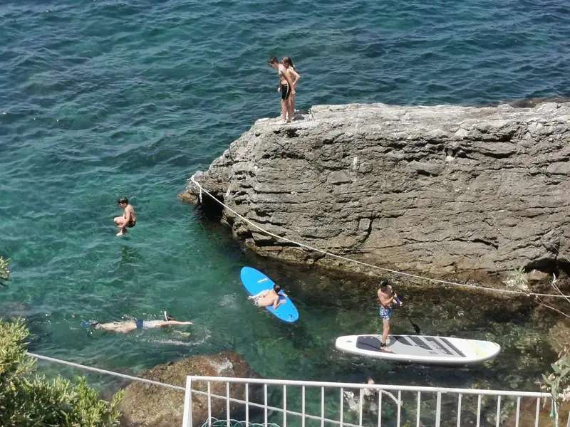 Swimmers and paddle boards around a large flat rock