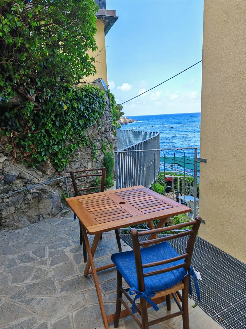Small wooden table and a blue chair in the sun by the railing